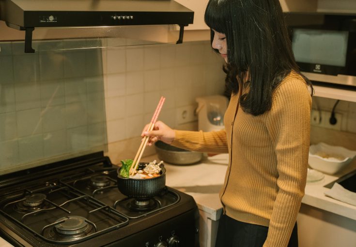 プロパンガス台で調理している黄色い服を着た若い女性