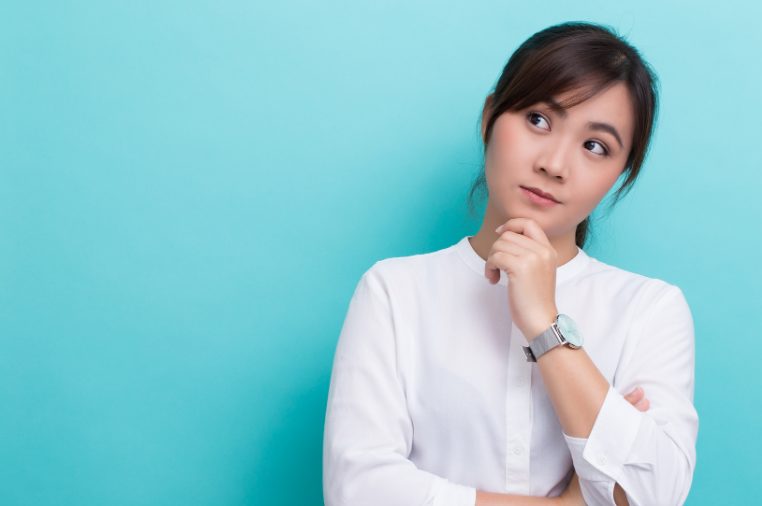 左手を顎に当て考えている白いシャツの若い女性