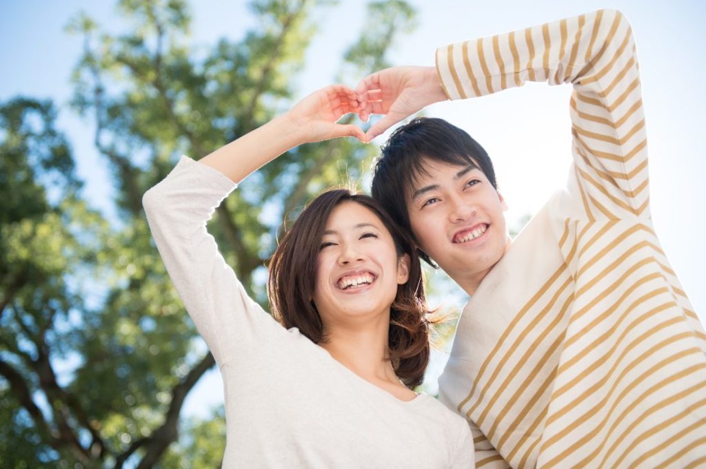 嬉しそうに微笑みながら互いの腕でハートマークを作り微笑んでいるカップル