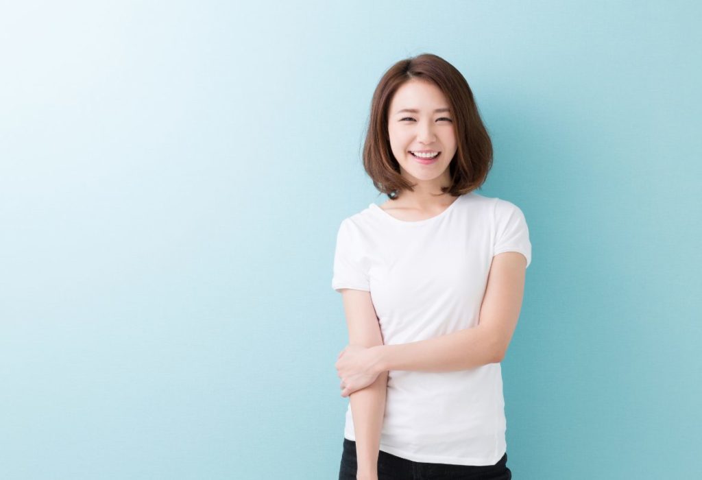 左手で右腕をつかんで微笑む白いTシャツの女性