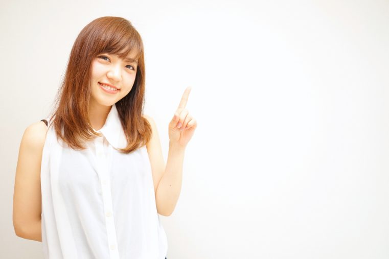 左手人差し指を差し出して笑顔で微笑む白いワンピースの若い女性