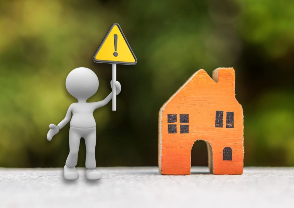 おもちゃの木の家の横で、注意マークを掲げている人形