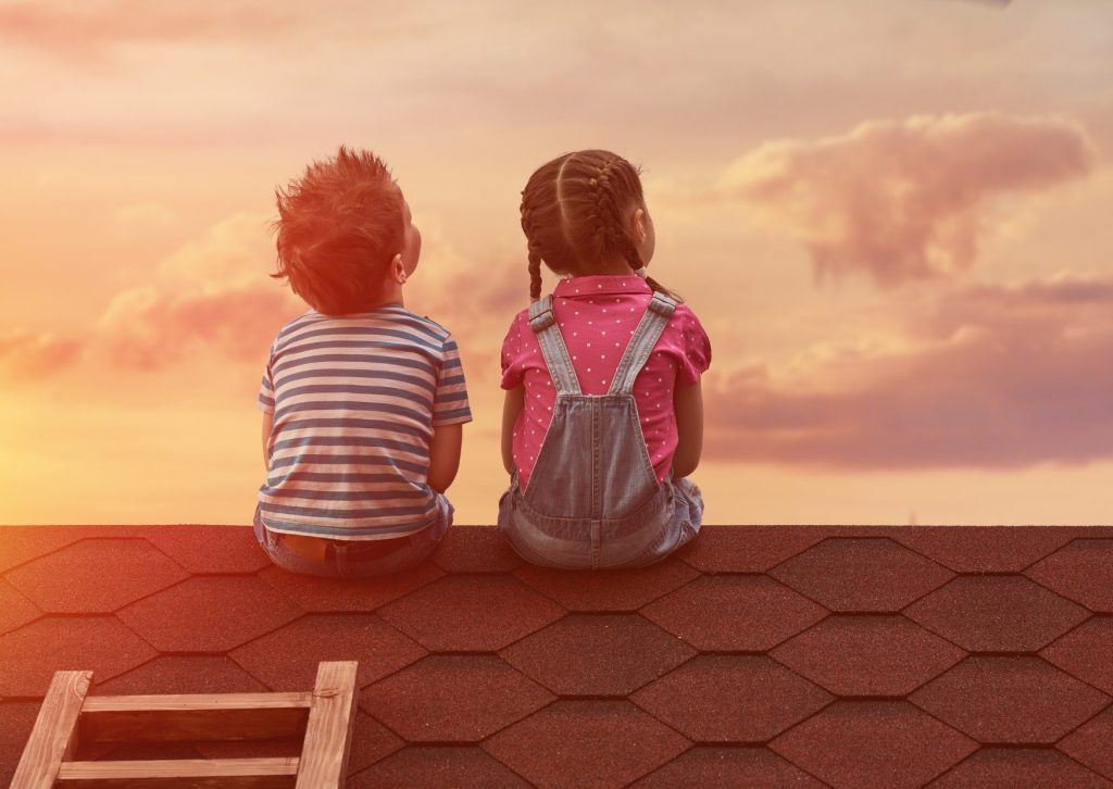 屋根に座って夕焼け空を見上げる男女の子供