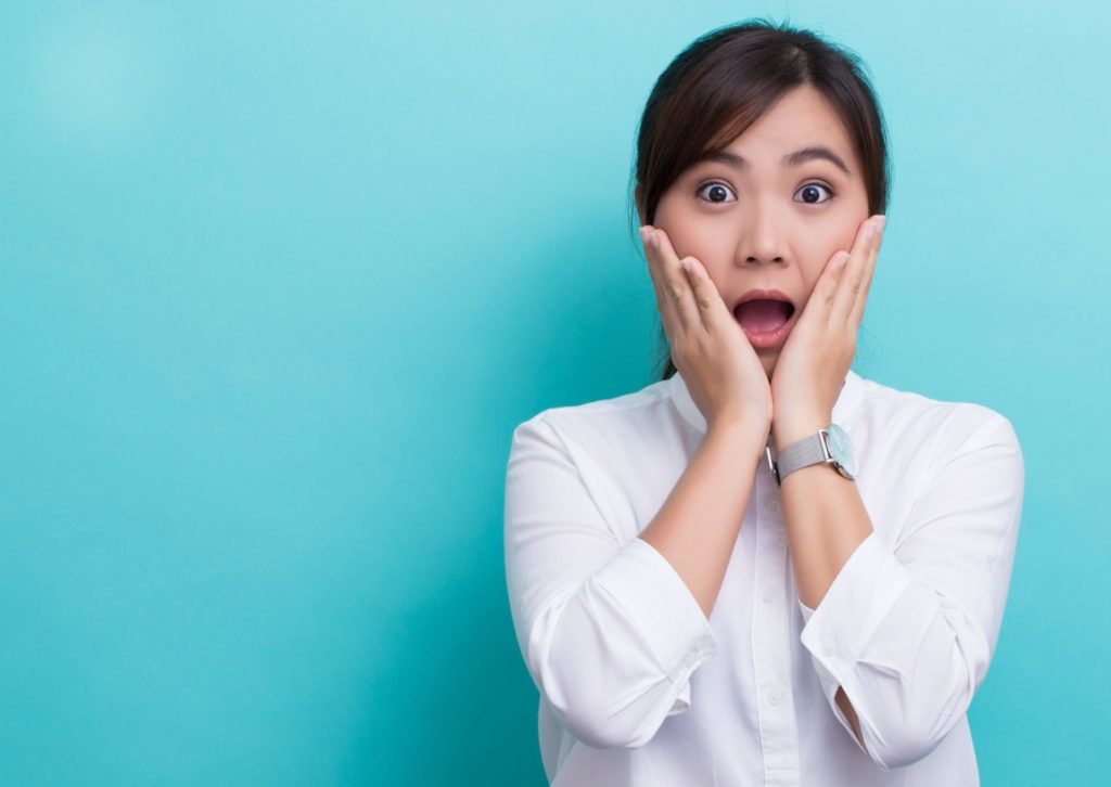 青い背景で両手を頬に当て口を開け目を見開いている若い女性