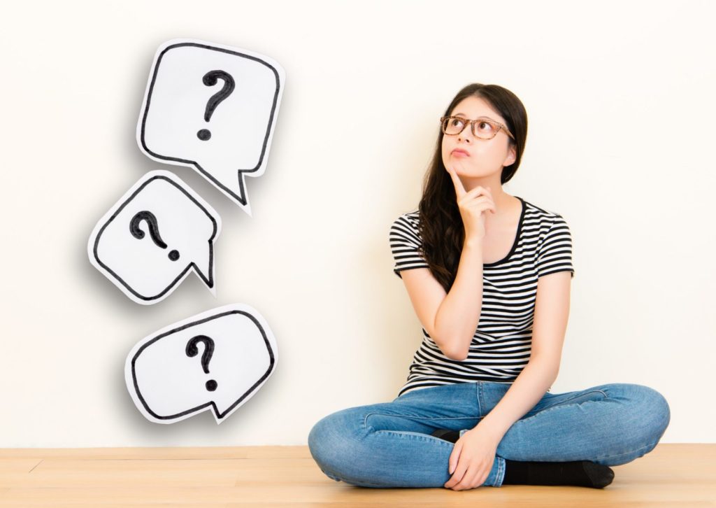 横ストライプのTシャツの若い女性が右人差し指を顎に当て、上を向いて感がいている。横に？マークのイラスト