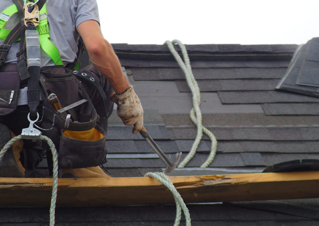 屋根に乗って修理している金づちを持った業者