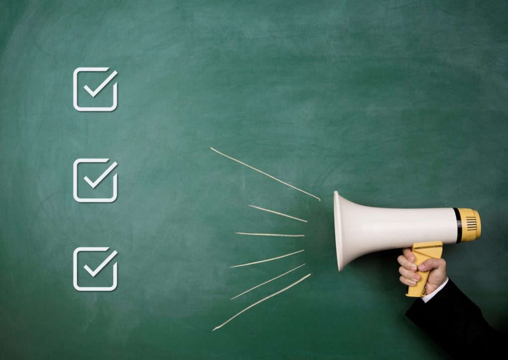 黒板に書かれたチェックマークの前で拡声器を持っている人の腕