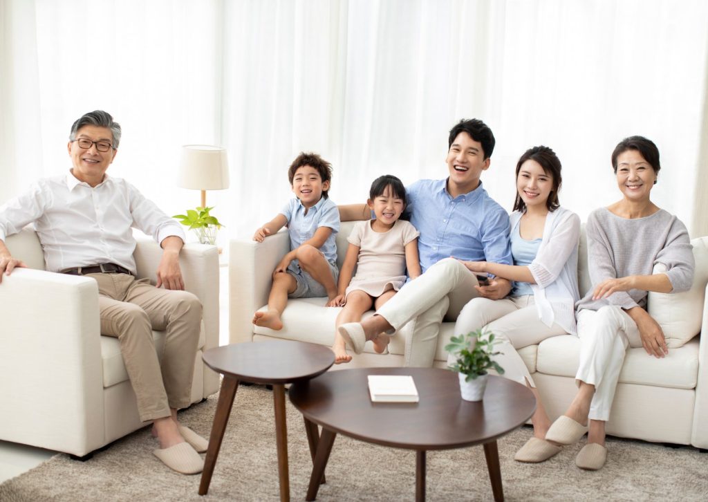 ２人の男女の子供を囲んでパパ、ママ、バアバ、ジイジがリビングのソファーに皆笑顔で座っている