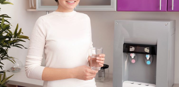 ウォーターサーバーの前でコップに入った水を持ち微笑む女性