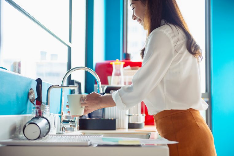 水道水をコップに注いでいる笑顔の白シャツの若い女性