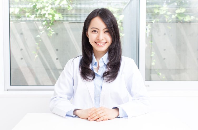 テーブルの前に笑顔で座る白衣の髪の長い若い女性のイメージ